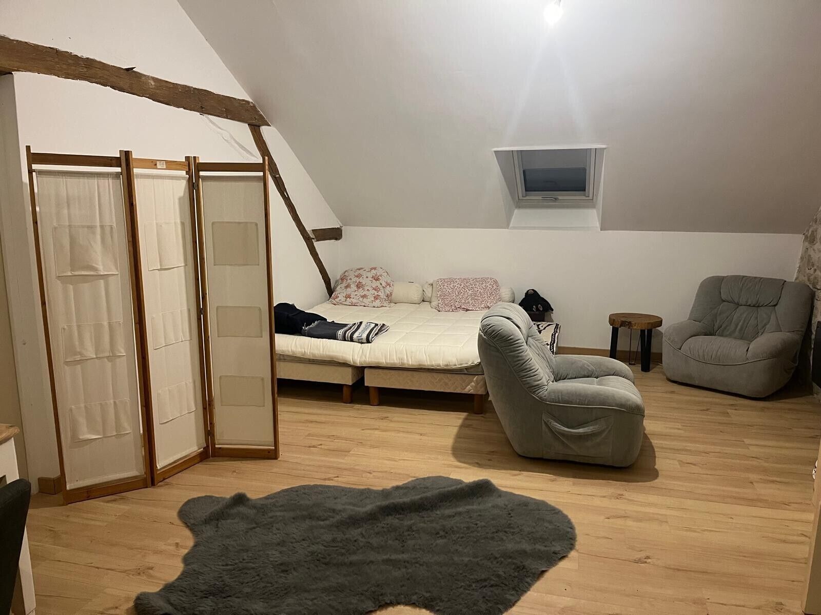 A bedroom with a loft bed, a grey armchair, a small table, and a TV on the wall.