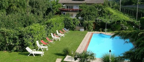 Una piscina con sillas de descanso, una casa y un paisaje montañoso de fondo.