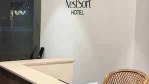 Un mostrador de recepción con el logotipo del Hotel NestSort, una silla de madera y un teléfono instalado en la pared.