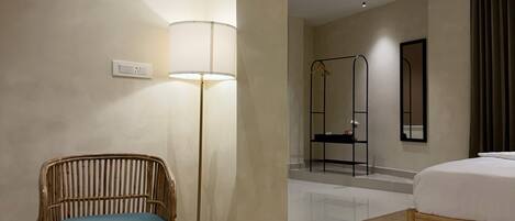 A hotel room with a bed, a chair, a floor lamp, a mirror, and a wardrobe.