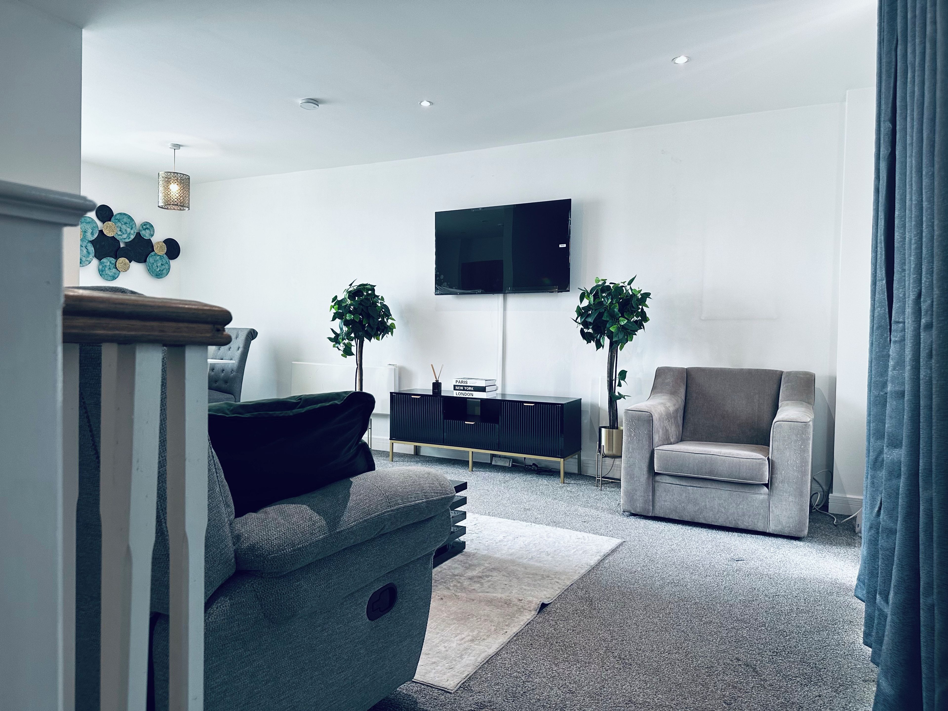 Ein modernes Wohnzimmer mit einem grauen Sofa, einer schwarzen Unterhaltungseinheit, einem Flachbildfernseher und zwei Blumentöpfen.