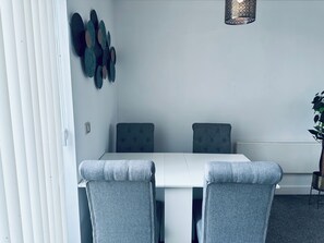 A dining area with a white table, grey upholstered chairs, and a decorative wall hanging. - Modern2 Bedroom Apartment/private Parking /sleep 5/balcony View in Birmingham City Centre (Birmingham)