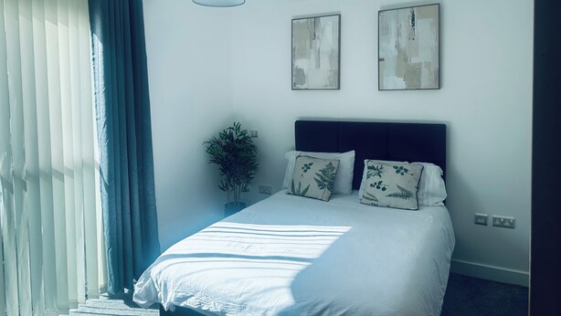 Une chambre à coucher comprenant un lit, un ventilateur de plafond, une fenêtre avec des rideaux et deux œuvres d’art accrochées au mur.