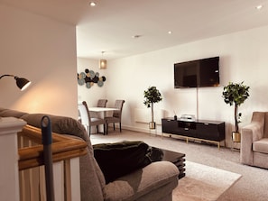 A modern living room with a sofa, a coffee table, a dining area with chairs, a TV mounted on the wall, and two potted plants. - Modern2 Bedroom Apartment/private Parking /sleep 5/balcony View in Birmingham City Centre (Birmingham)