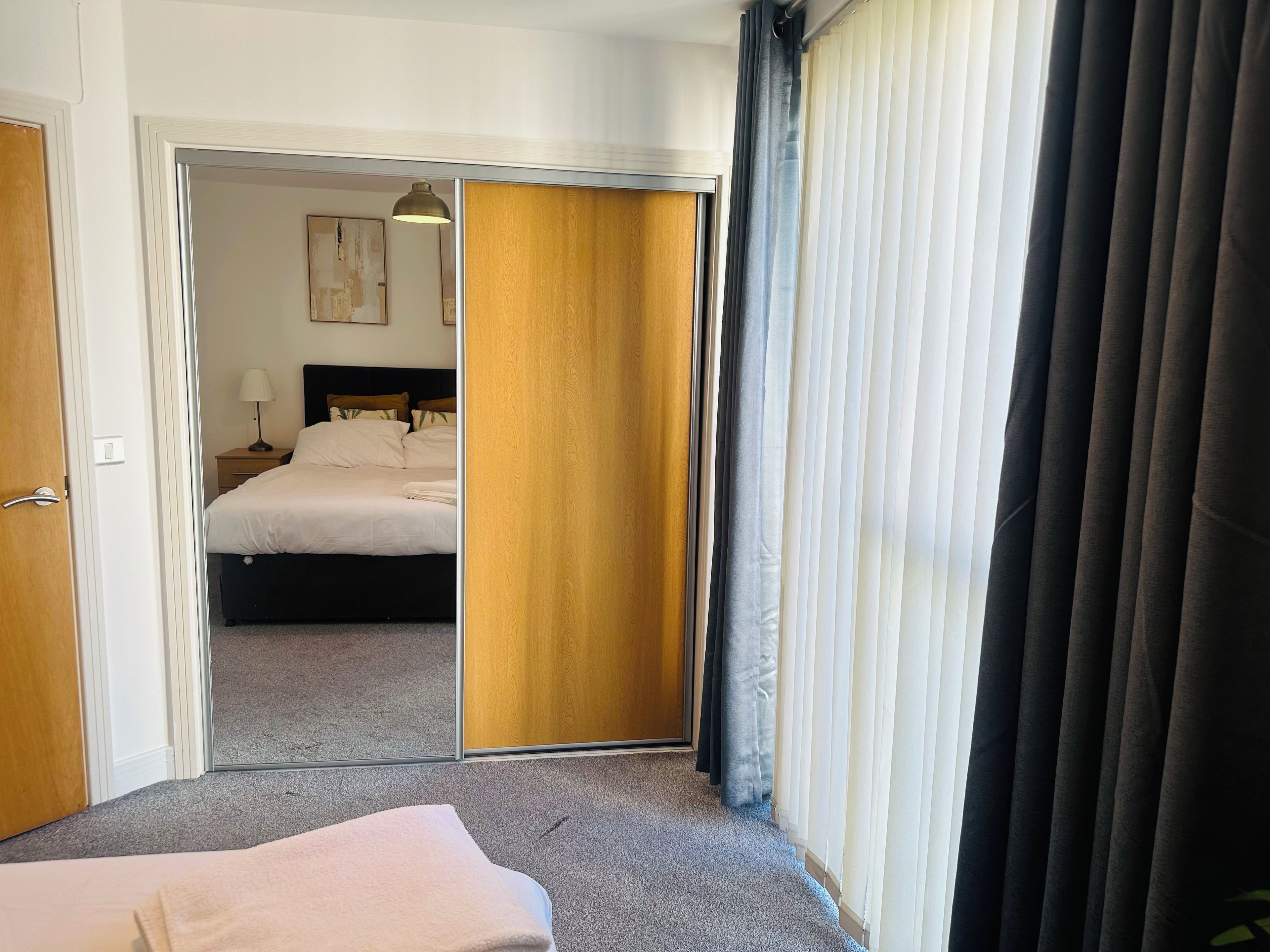 A hotel room with a bed, a nightstand, a lamp, and a view through a sliding door.