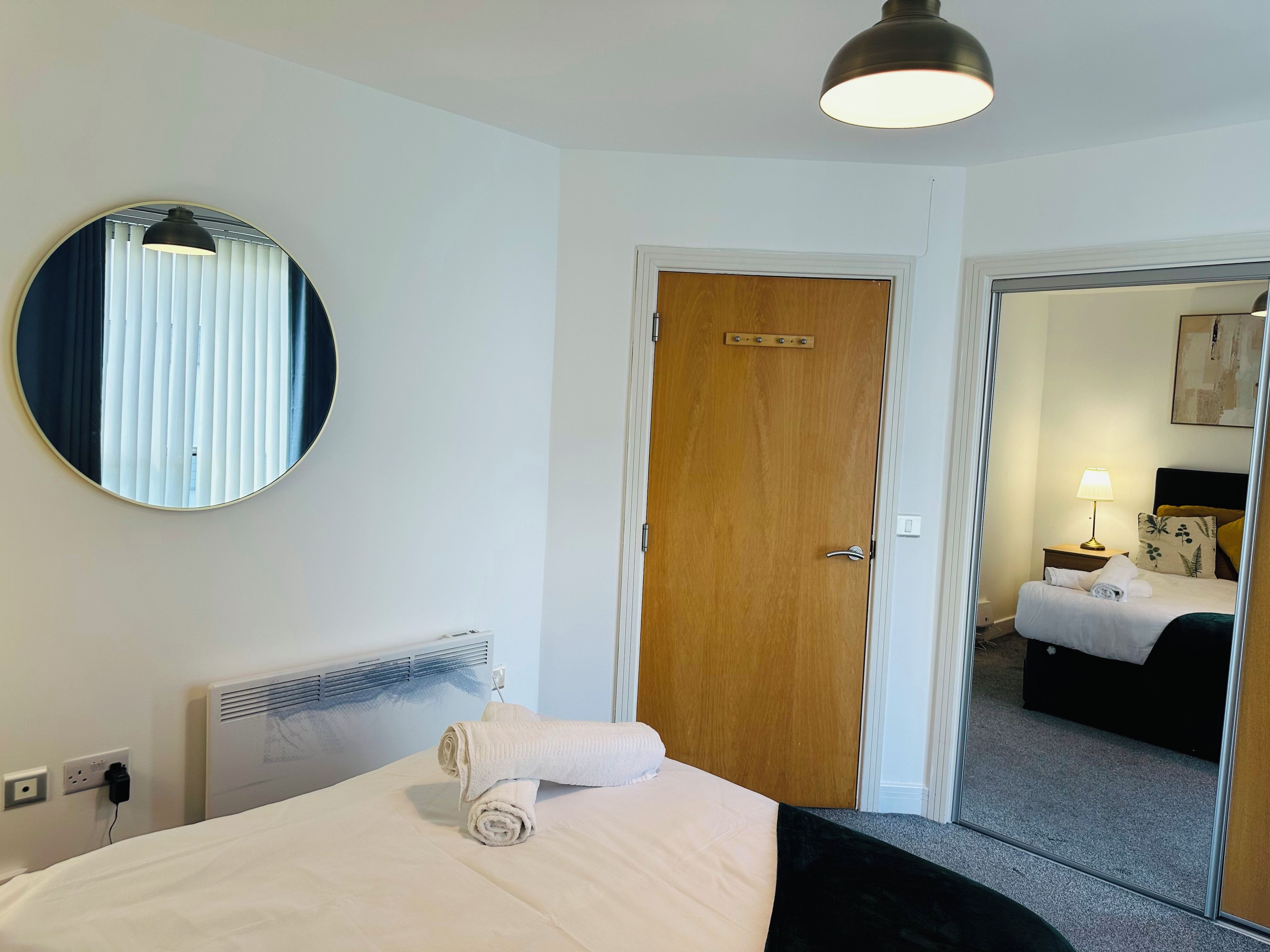 Una habitación de hotel con una cama, un espejo redondo, una puerta y vistas a otra habitación.