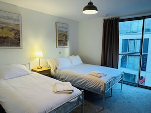 A hotel room with two beds, a bedside lamp, and a large window with curtains.