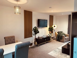 A modern living room with a sofa, a dining table, and a TV mounted on the wall.