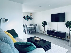 A modern living room with a sofa, coffee table, and a dining area with chairs and a table. - Modern2 Bedroom Apartment/private Parking /sleep 5/balcony View in Birmingham City Centre (Birmingham)