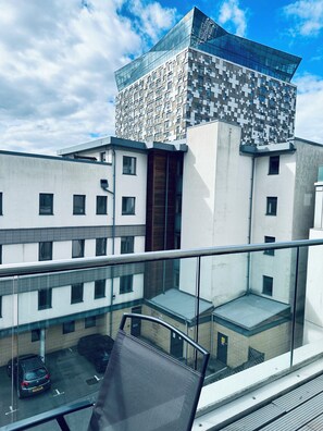 A modern building with a distinctive geometric facade, a balcony with a metal railing, and a parked car below. - Modern2 Bedroom Apartment/private Parking /sleep 5/balcony View in Birmingham City Centre (Birmingham)