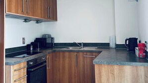 Une cuisine compacte dotée de meubles en bois, d’un four encastré, d’un four à micro-ondes et d’une machine à café.