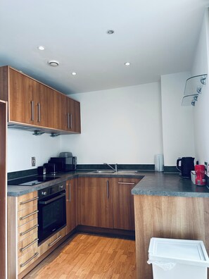 A compact kitchen with wooden cabinets, a built-in oven, a microwave, and a coffee maker. - Modern2 Bedroom Apartment/private Parking /sleep 5/balcony View in Birmingham City Centre (Birmingham)