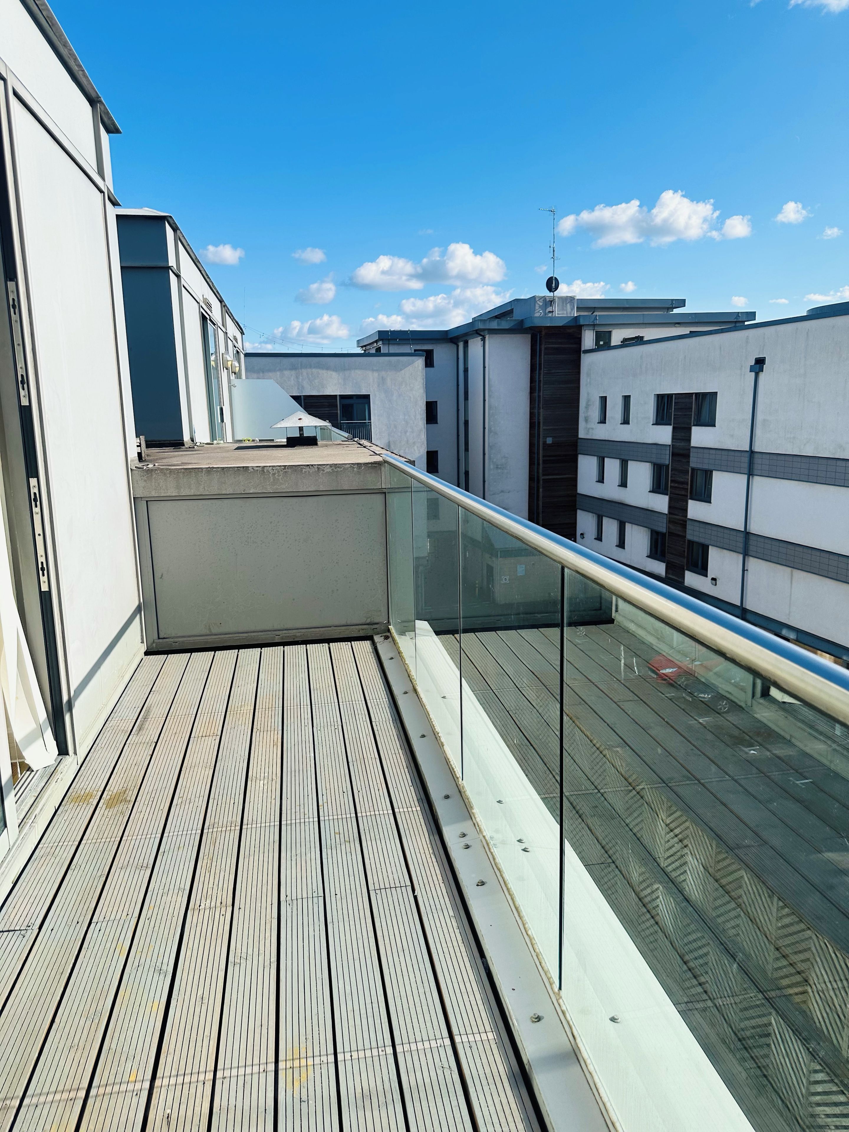 Une terrasse sur le toit, dotée d’une plateforme en bois, d’une balustrade en verre et offrant une vue sur un ciel bleu dégagé.