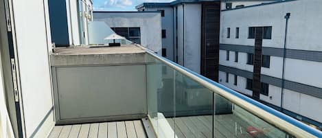 Une terrasse sur le toit, dotée d’une plateforme en bois, d’une balustrade en verre et offrant une vue sur un ciel bleu dégagé.