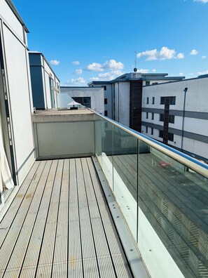 A rooftop terrace with a wooden deck, glass balustrade, and a clear blue sky. - Modern2 Bedroom Apartment/private Parking /sleep 5/balcony View in Birmingham City Centre (Birmingham)