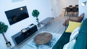 Een woonkamer met een televisie, bank, salontafel en een eethoek met stoelen.