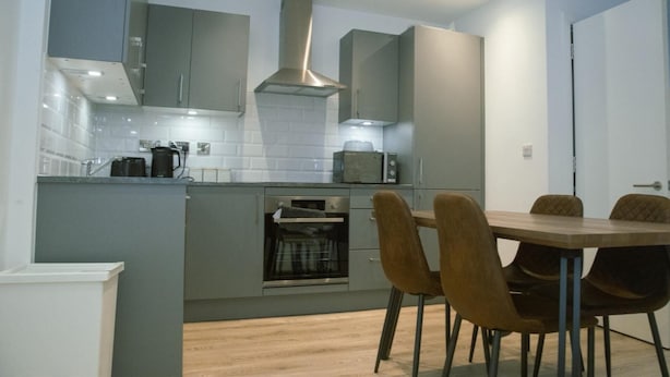 Een moderne keuken met grijze kastjes, een inbouwoven, een magnetron en een eettafel met vier stoelen.
