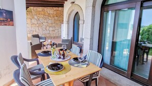 Un área de comedor al aire libre con pared de piedra, techo de madera y ventanas amplias.