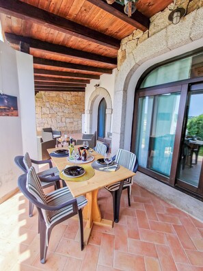 An outdoor dining area with a stone wall, wooden ceiling, and large windows. - Villa Corallo, entire villa 4km from Alghero with breathtaking views of Capo Caccia (Sardegna)