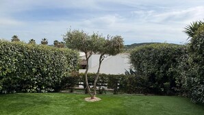 Un jardín bien cuidado con un árbol central, rodeado de setos podados y un césped impecable.