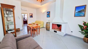 Una sala de estar con sofá, mesa de comedor, sillas, chimenea y cocina al fondo.