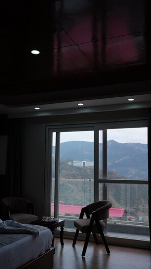 A bedroom with a large window, a bed, a chair, and a small table. - The Heaven Paradise Premium (Shimla)