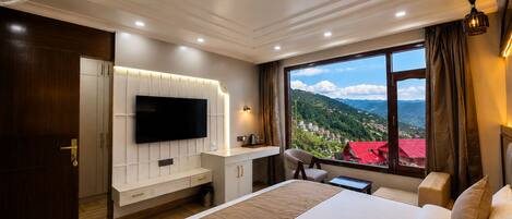 A hotel room with a large bed, a TV mounted on the wall, a desk with a chair, and a window with a view of a mountainous landscape.
