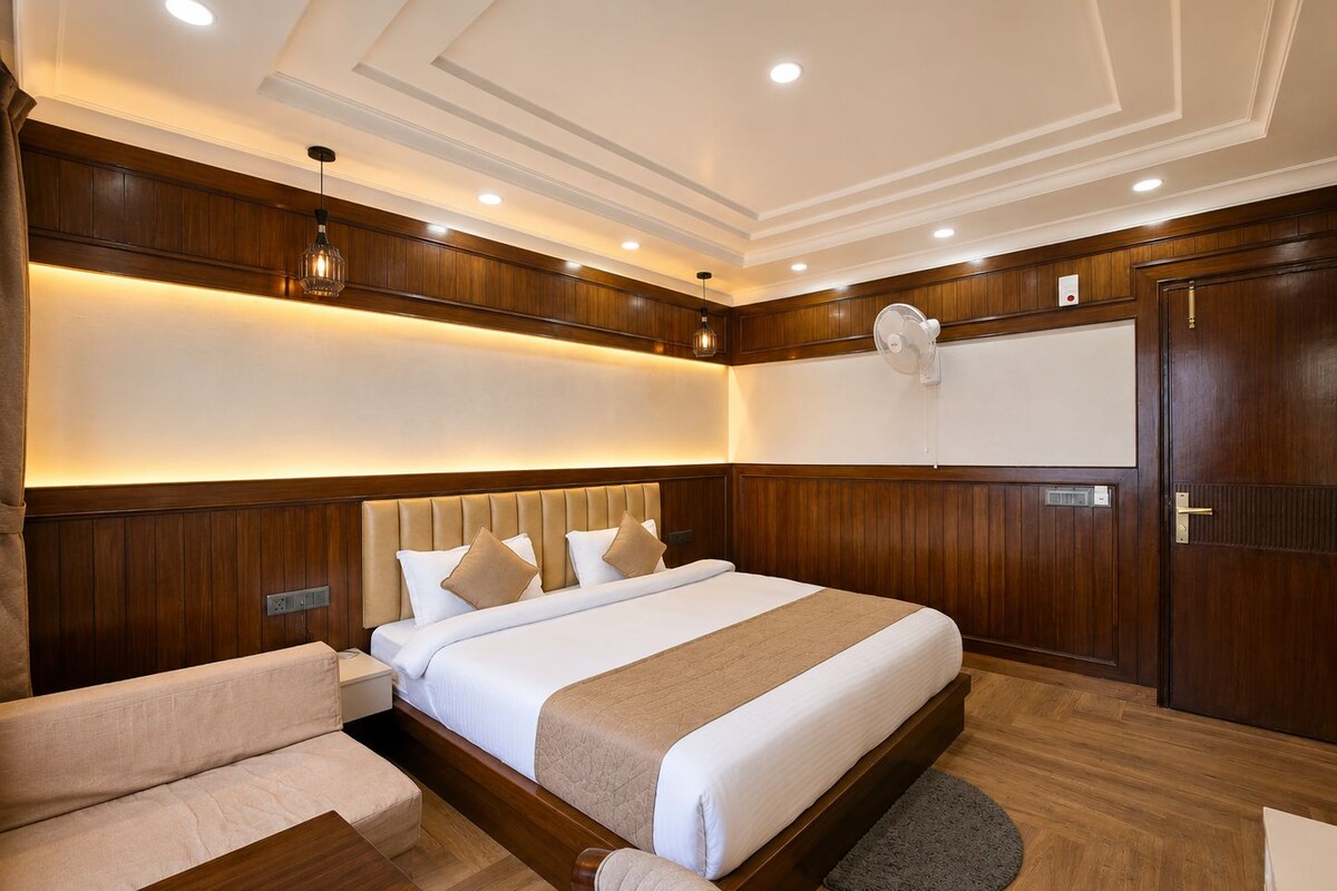 A hotel room with a large bed, a sofa, a desk, and a fan.