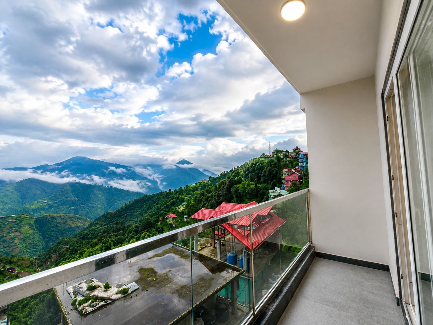 A balcony with a glass railing overlooking a mountainous landscape with houses.