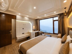 A hotel room with a large bed, a desk with a chair, a wardrobe, and a view of the mountains through the window. - The Heaven Paradise Premium (Shimla)
