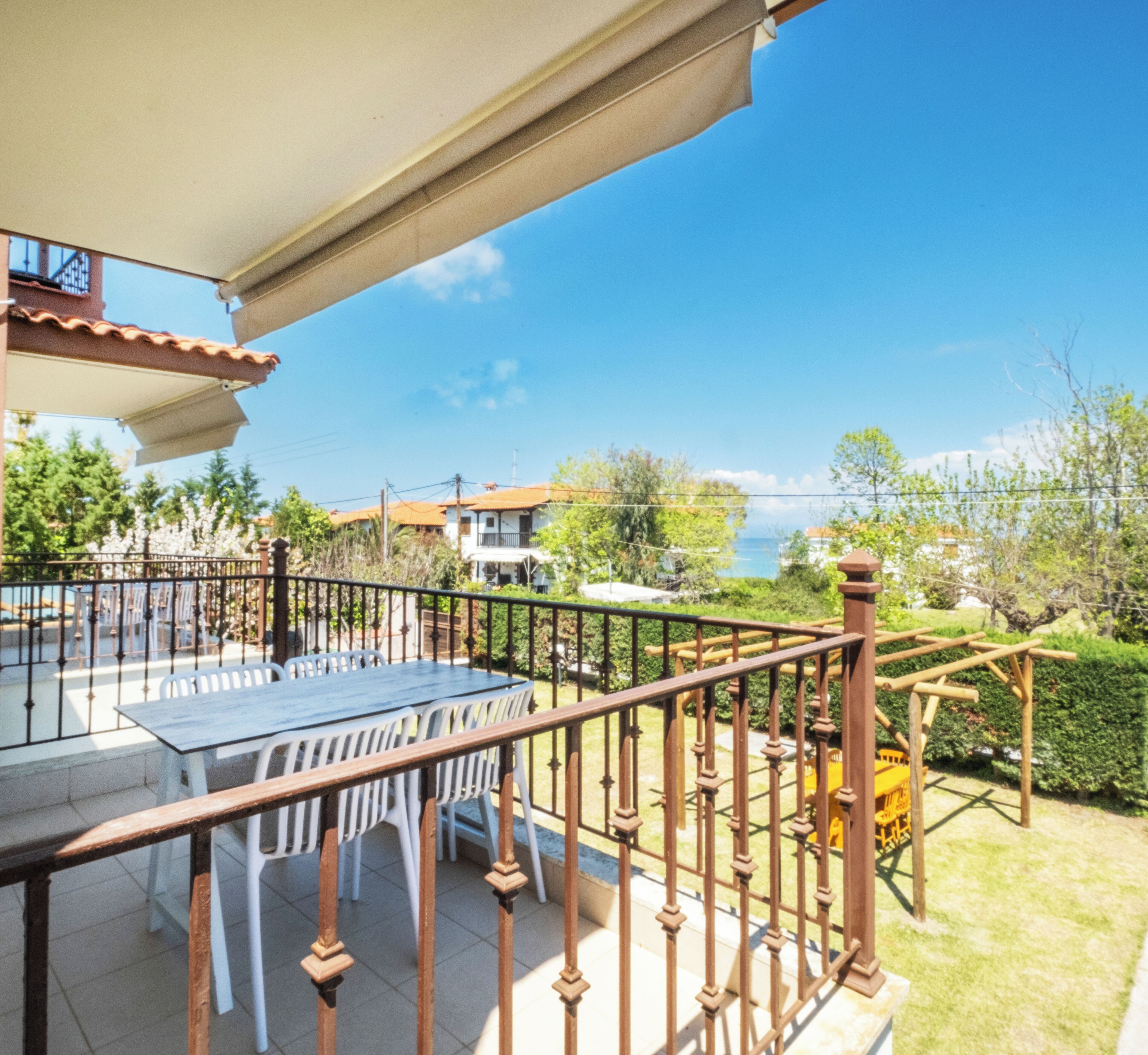 Ein Balkon mit Tisch, Stühlen, Geländer und Blick auf das Meer und Gebäude.