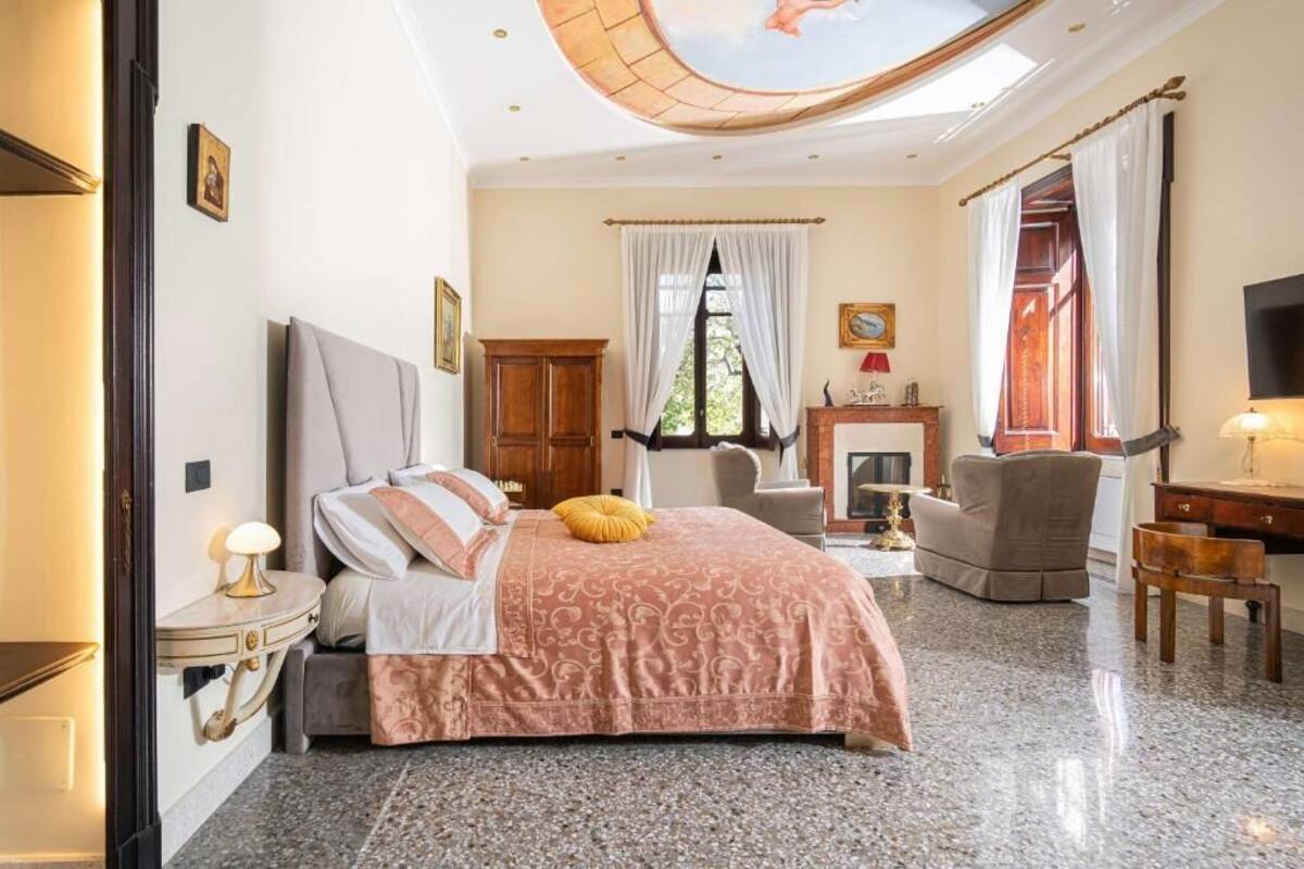 A bedroom with a bed, a desk, a chair, a fireplace, and a ceiling with a skylight.