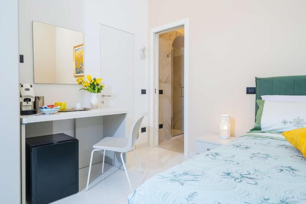 A bedroom with a bed, bedside table, lamp, and a desk with chair.