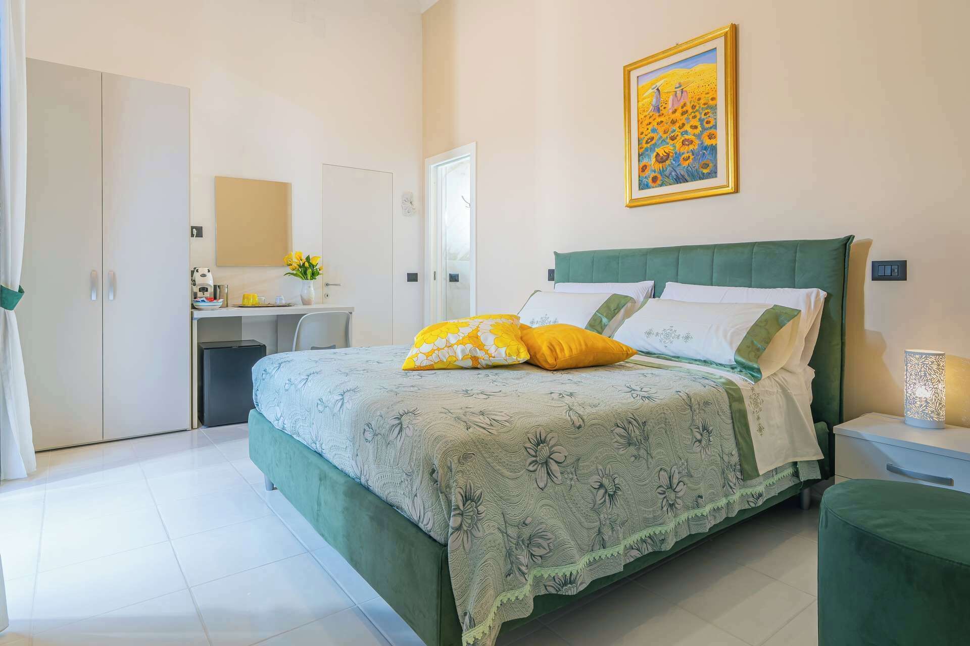 A bedroom with a bed, bedside table, lamp, and a painting on the wall.