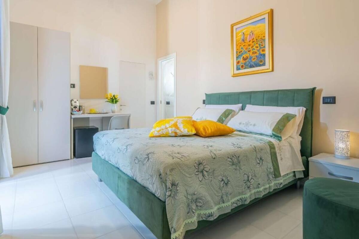 A bedroom with a bed, a nightstand, a desk, a chair, a wardrobe, and a painting on the wall.