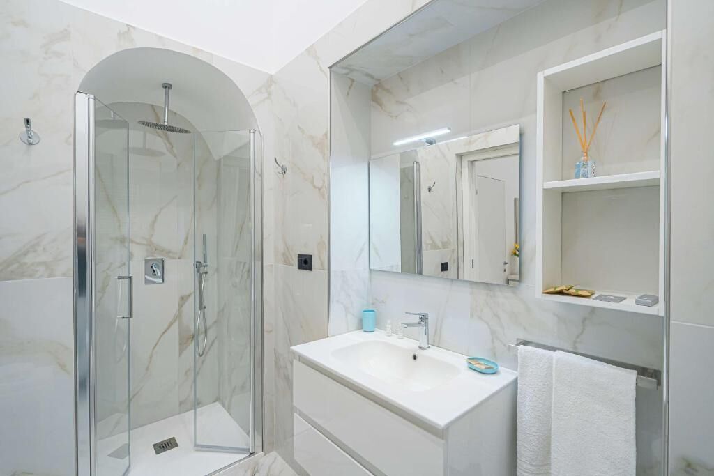 Un bany modern amb dutxa d'acer vitrit, un lavabo blanc i un mirall per sobre.