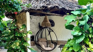 A thatched-roof structure with a hanging chair and lush green foliage. - Beautiful 1-bedroom villa with AC in Diani, close to the airport and the beach (Kwale county)