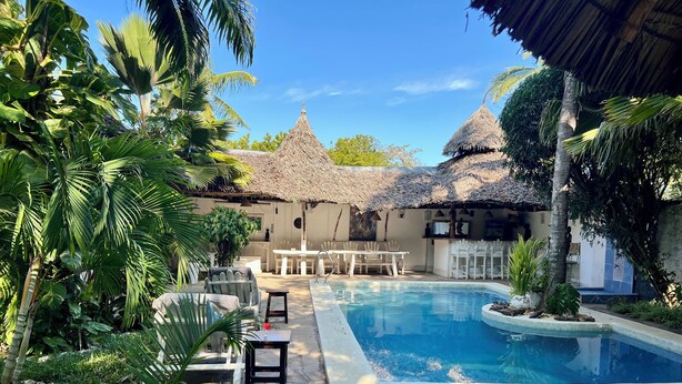A pool area with a thatched-roof structure, lounge chairs, and a dining table. - Beautiful 1-bedroom villa with AC in Diani, close to the airport and the beach (Kwale county)