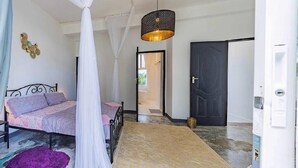 A bedroom with a bed, a canopy, a hanging light fixture, a door, and a hallway. - Beautiful 1-bedroom villa with AC in Diani, close to the airport and the beach (Kwale county)