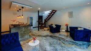 A modern living room with a kitchen area, a staircase, and blue upholstered furniture. - Beautiful 1-bedroom villa with AC in Diani, close to the airport and the beach (Kwale county)