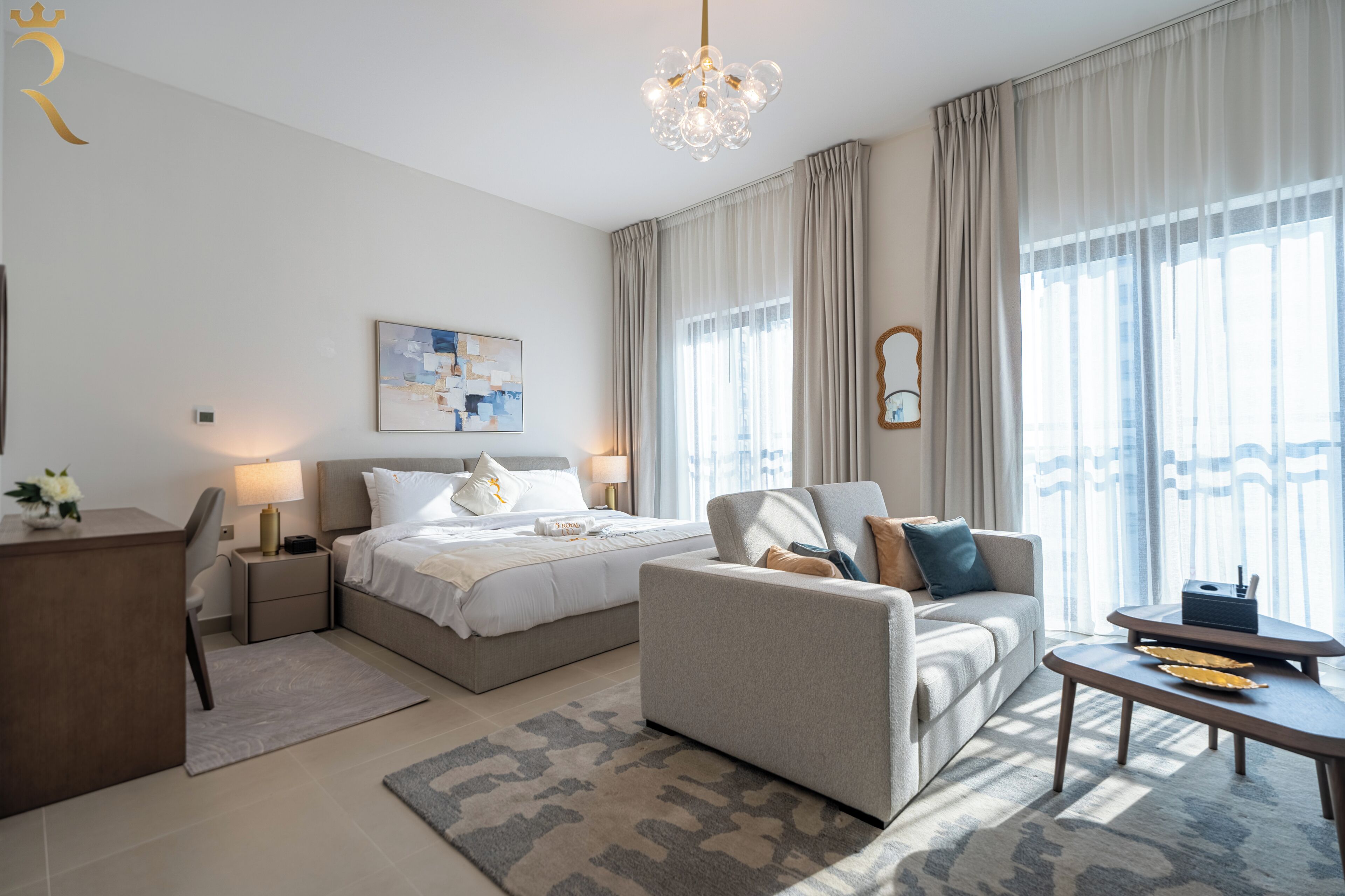 Una habitación de hotel moderna con cama, sofá, escritorio y un ventanal con cortinas.