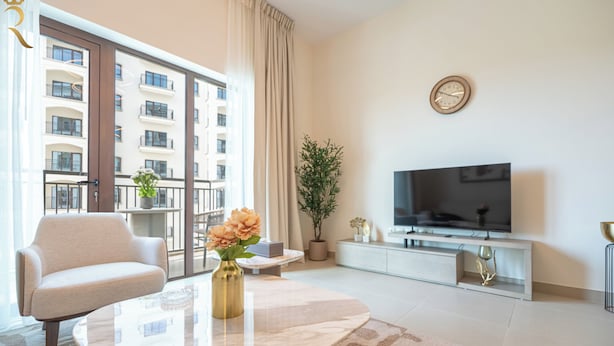 A modern living room with a sofa, a coffee table, a TV, and a large window with a view of a building. - Yas Golf Collection Apartments (Abu Dhabi)