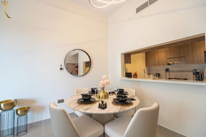 Un comedor moderno con una mesa redonda, sillas, un jarrón con flores y una cocina visible a través de un espacio abierto.