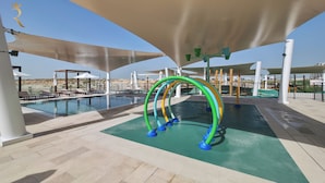 A pool area with lounge chairs, a children's play structure, and a view of the beach. - Yas Golf Collection Apartments (Abu Dhabi)