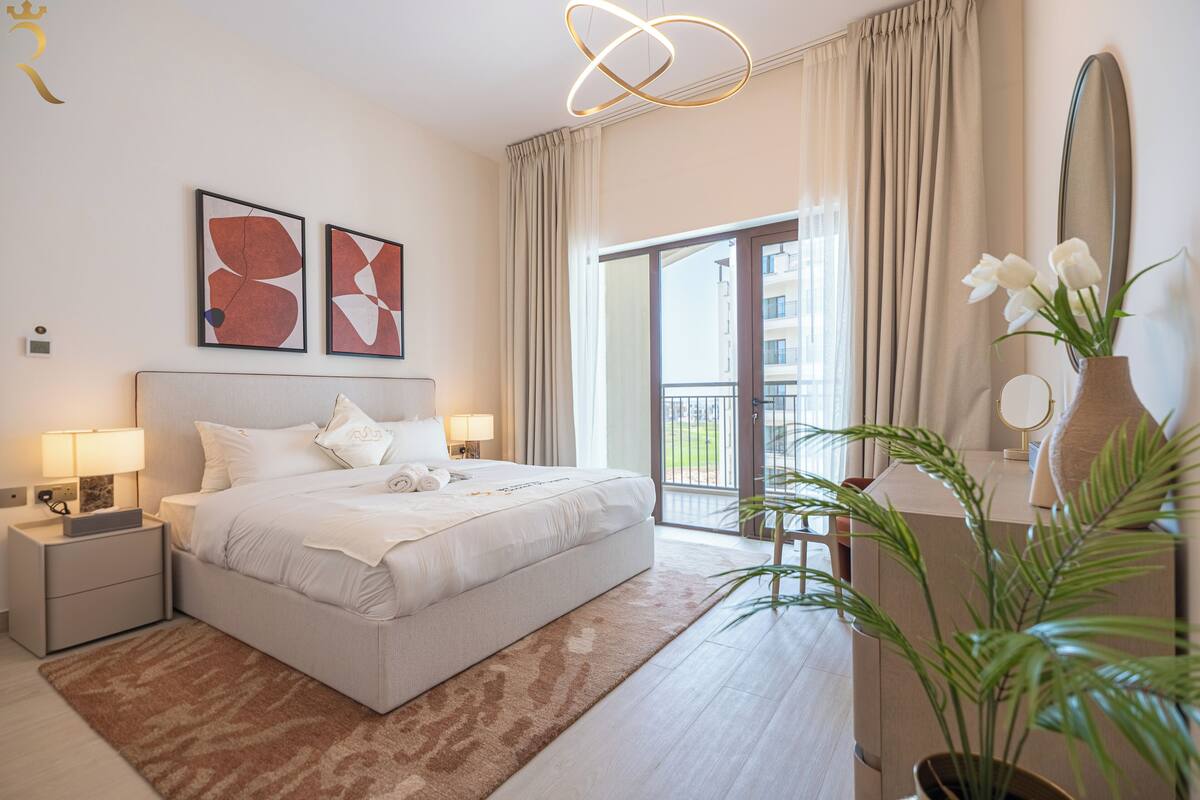 A hotel room with a bed, nightstands, a mirror, a vase with flowers, and a view of the outside.