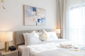 A hotel room with a bed, two bedside lamps, a nightstand, a framed abstract painting, and a window with curtains.