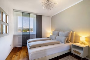 Une chambre moderne avec un grand lit, une table de chevet avec une lampe, une vue à travers une porte coulissante et un lustre.