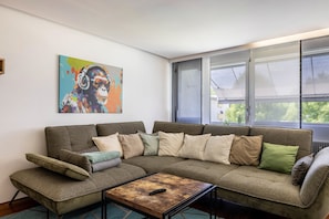 A modern living room with a sectional sofa, a coffee table, and a colorful abstract painting on the wall. - Apartment 'Cozy' with Mountain View, Private Terrace and Wi-Fi (Dornbirn)