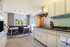 Une cuisine moderne avec un coin repas, de grandes fenêtres et une vue sur les immeubles.