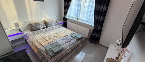 A modern bedroom with a bed, bedside table, TV, and a window with curtains.